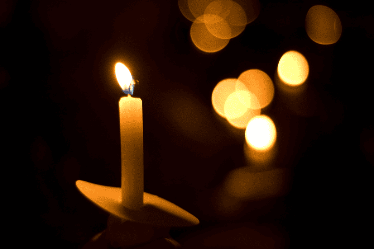 A single burning candle with other candles glowing in the background.