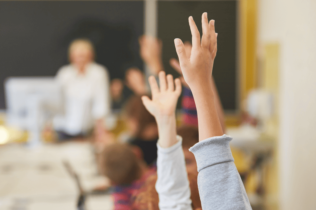 A group of kids with their hands in the air to ask questions.